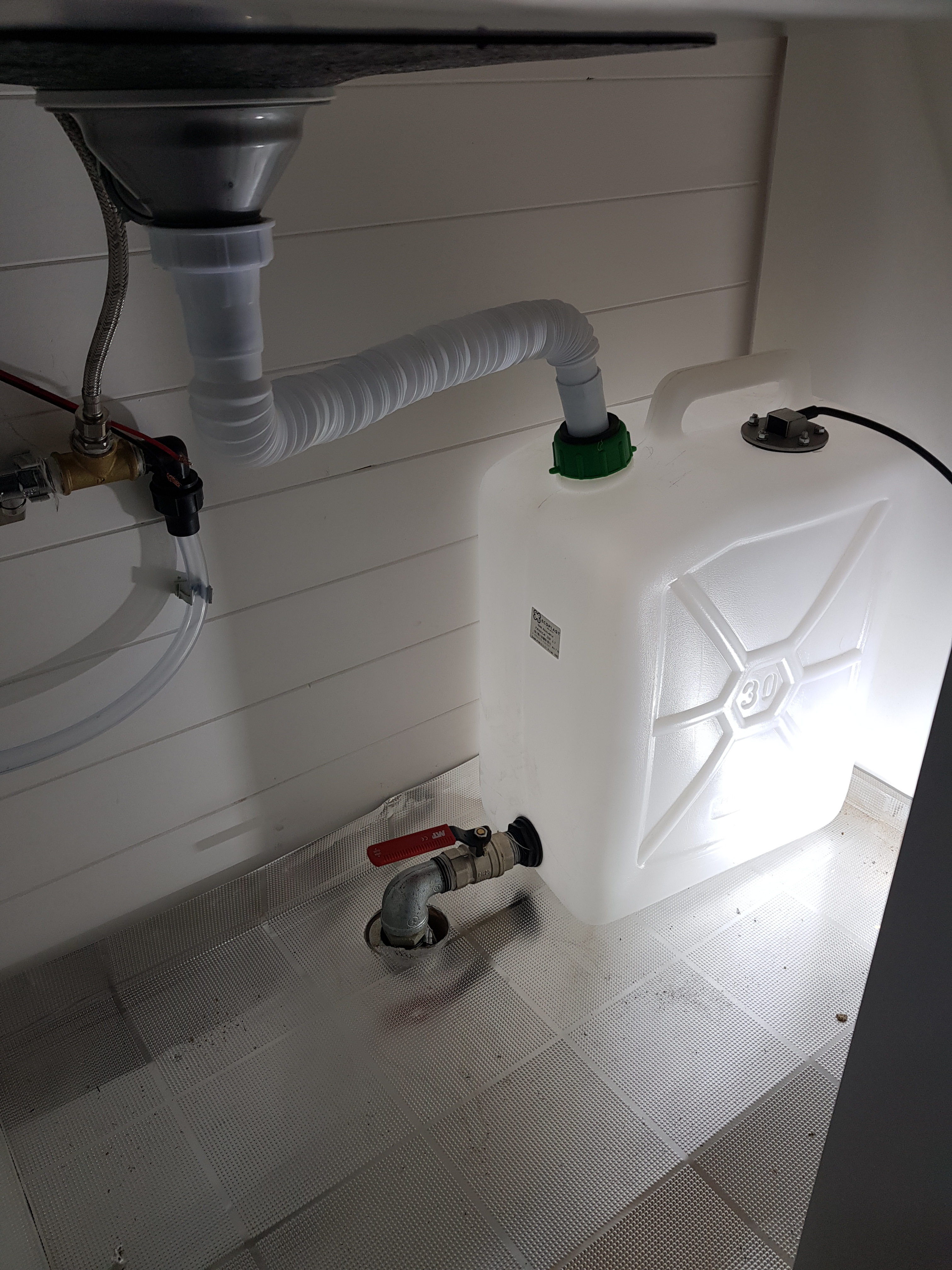 Water storage system inside the DIY Mercedes Sprinter camper van, featuring a 30-liter canister and plumbing setup.