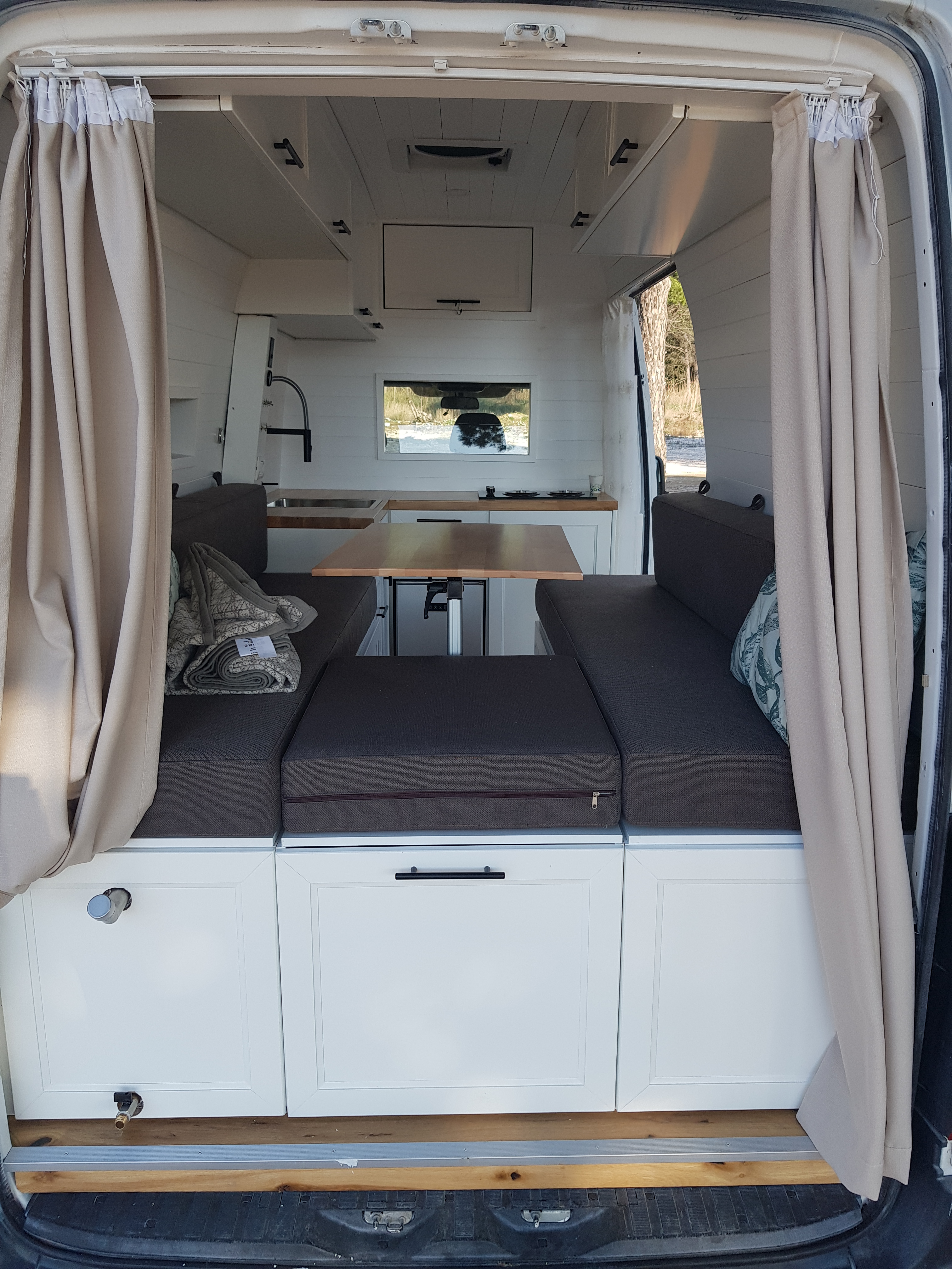 Interior view of the DIY Mercedes Sprinter camper van, showcasing a cozy living space with seating, a dining table, and kitchen amenities.