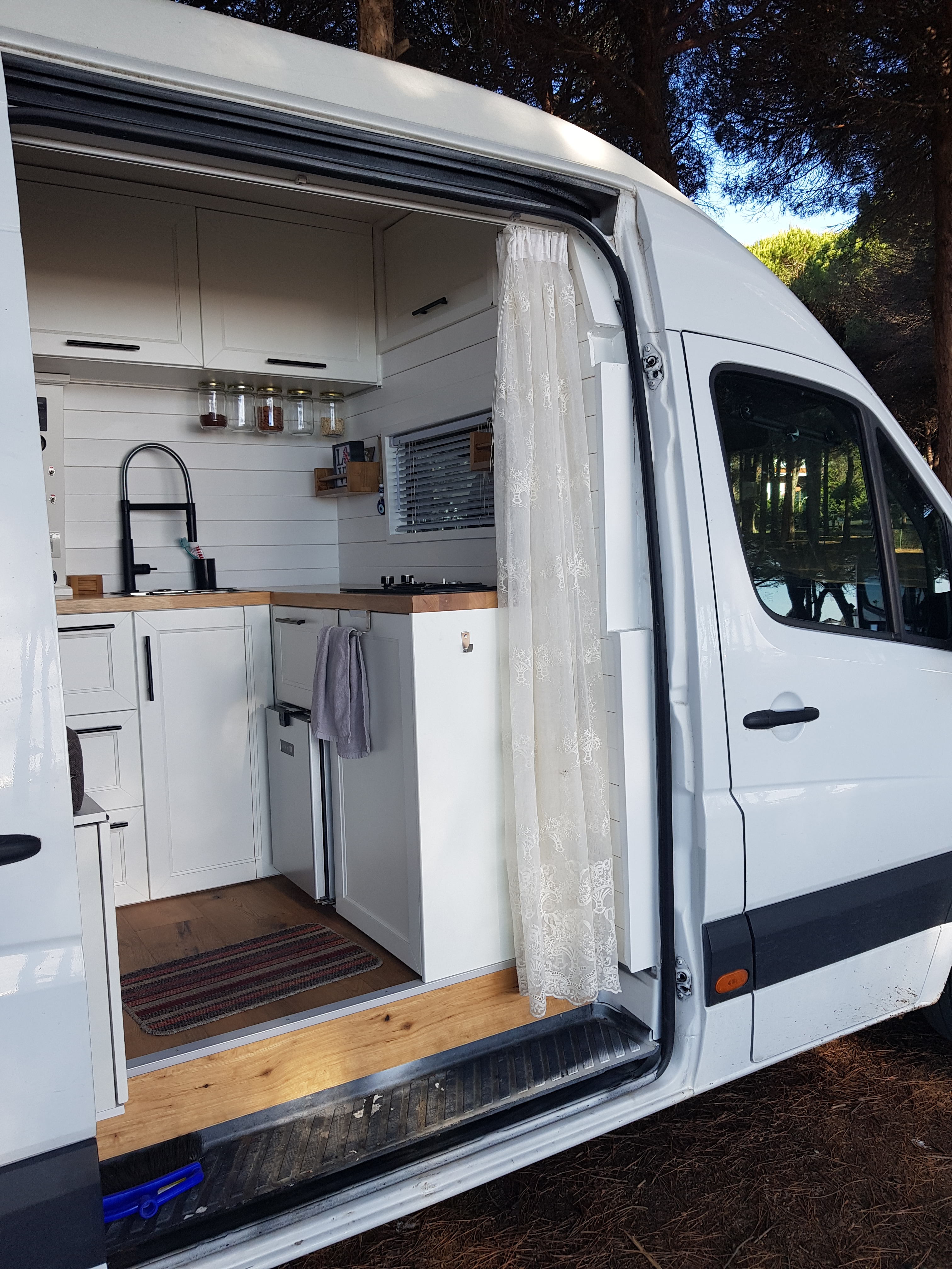 Interior view of a DIY Mercedes Sprinter camper van showcasing a compact kitchen, highlighted by a cozy design and functional features.