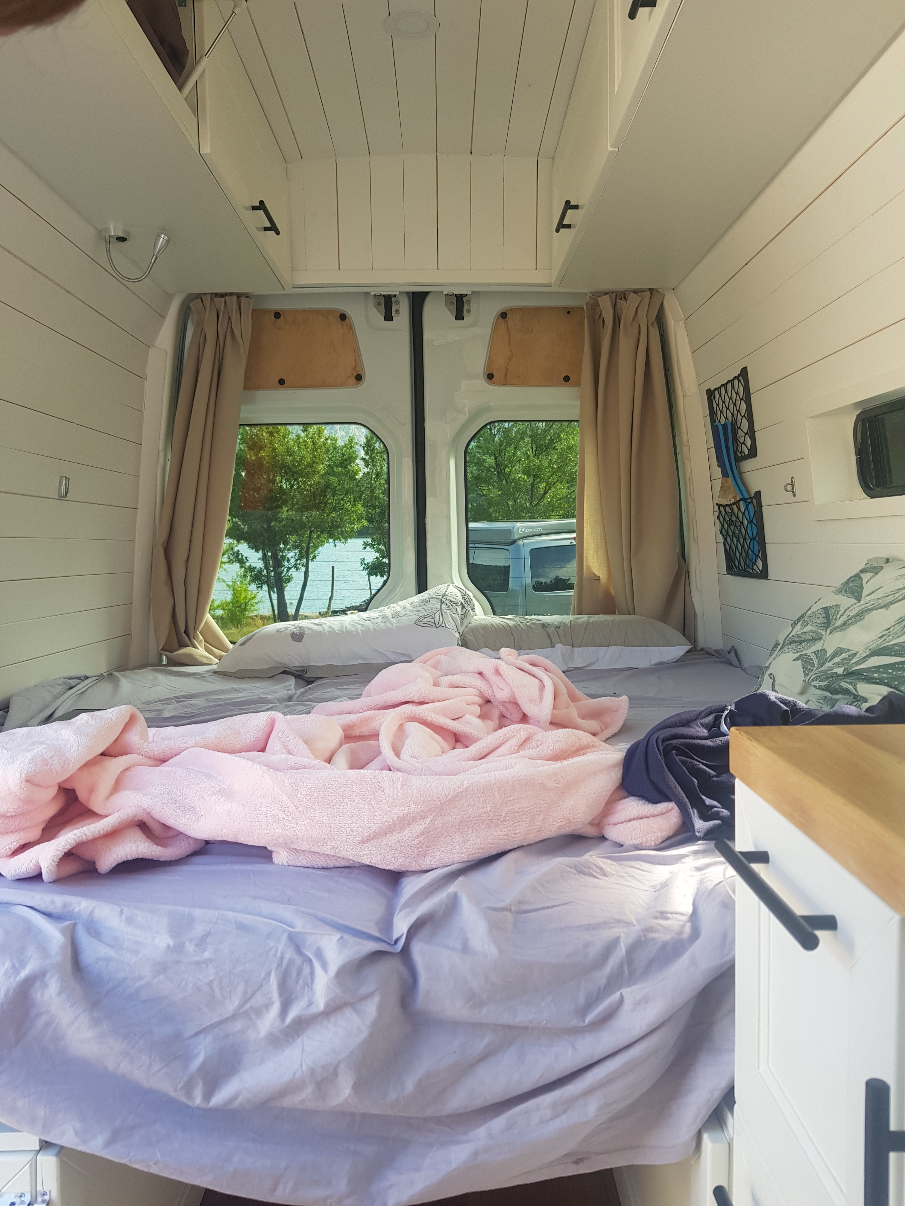 Cozy interior of the DIY Mercedes Sprinter camper van with a comfortable double bed and a view of nature outside.