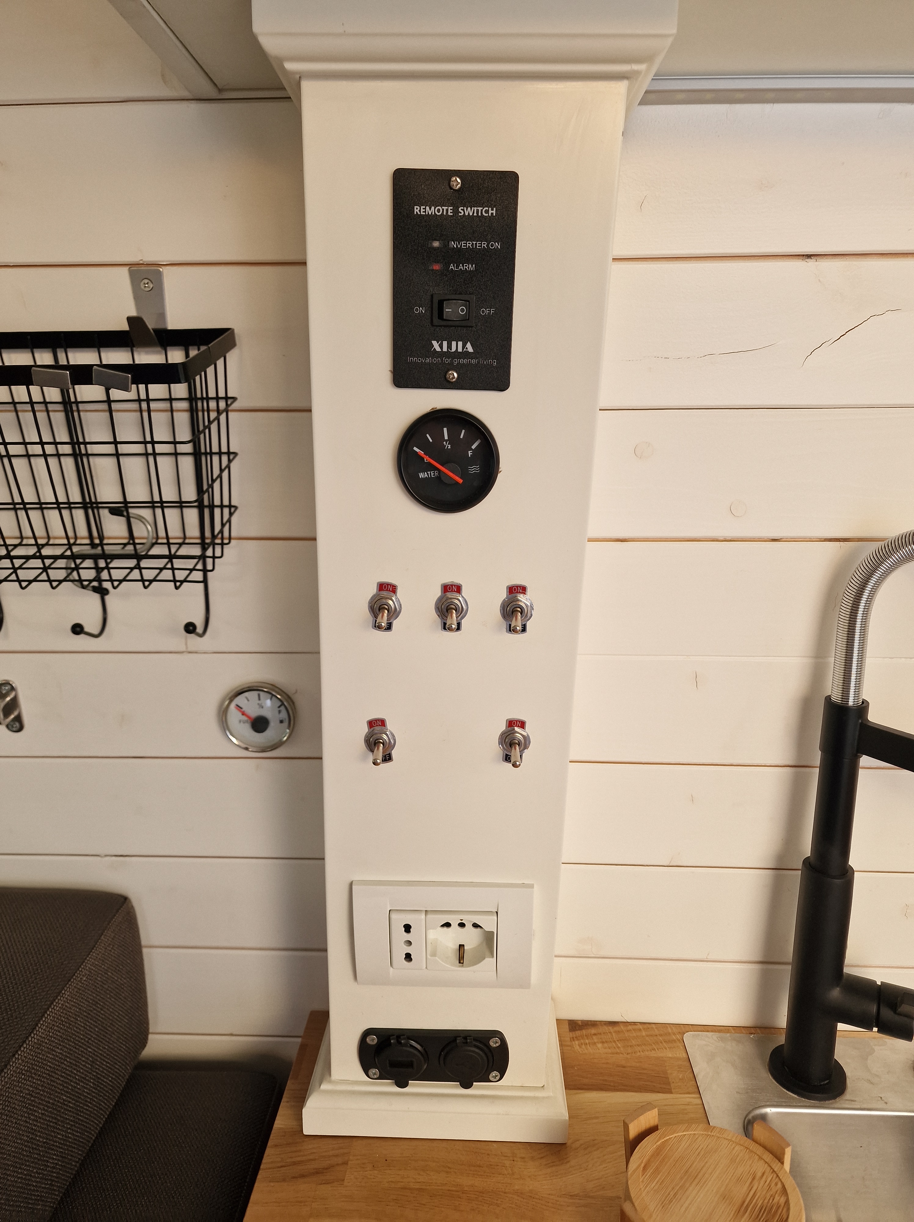 Control panel inside the DIY Mercedes Sprinter camper van featuring remote switch, water gauge, and multiple power outlets.