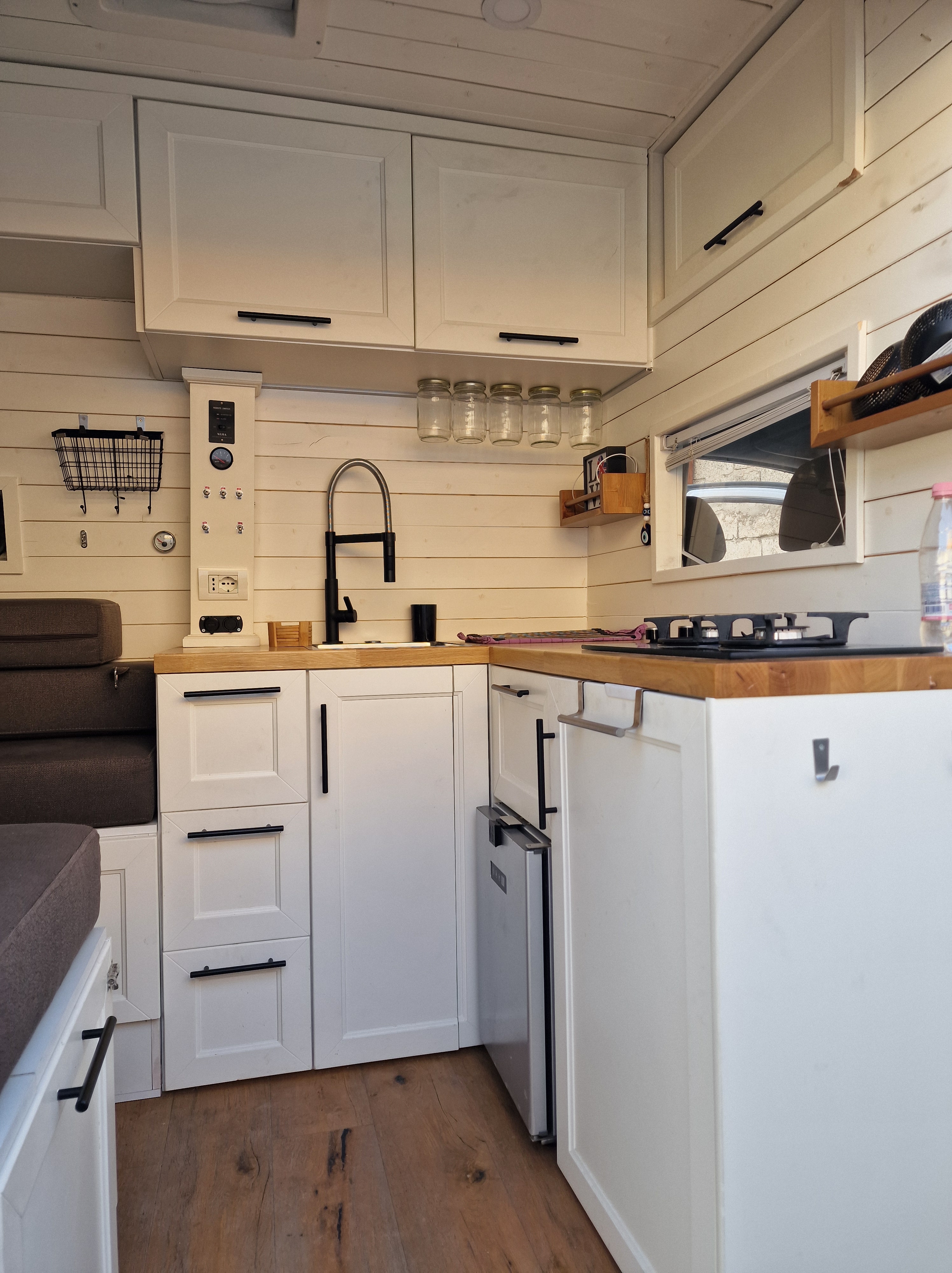 Interior view of a cozy kitchen in a DIY Mercedes Sprinter camper van, featuring a sink, stove, and storage space.